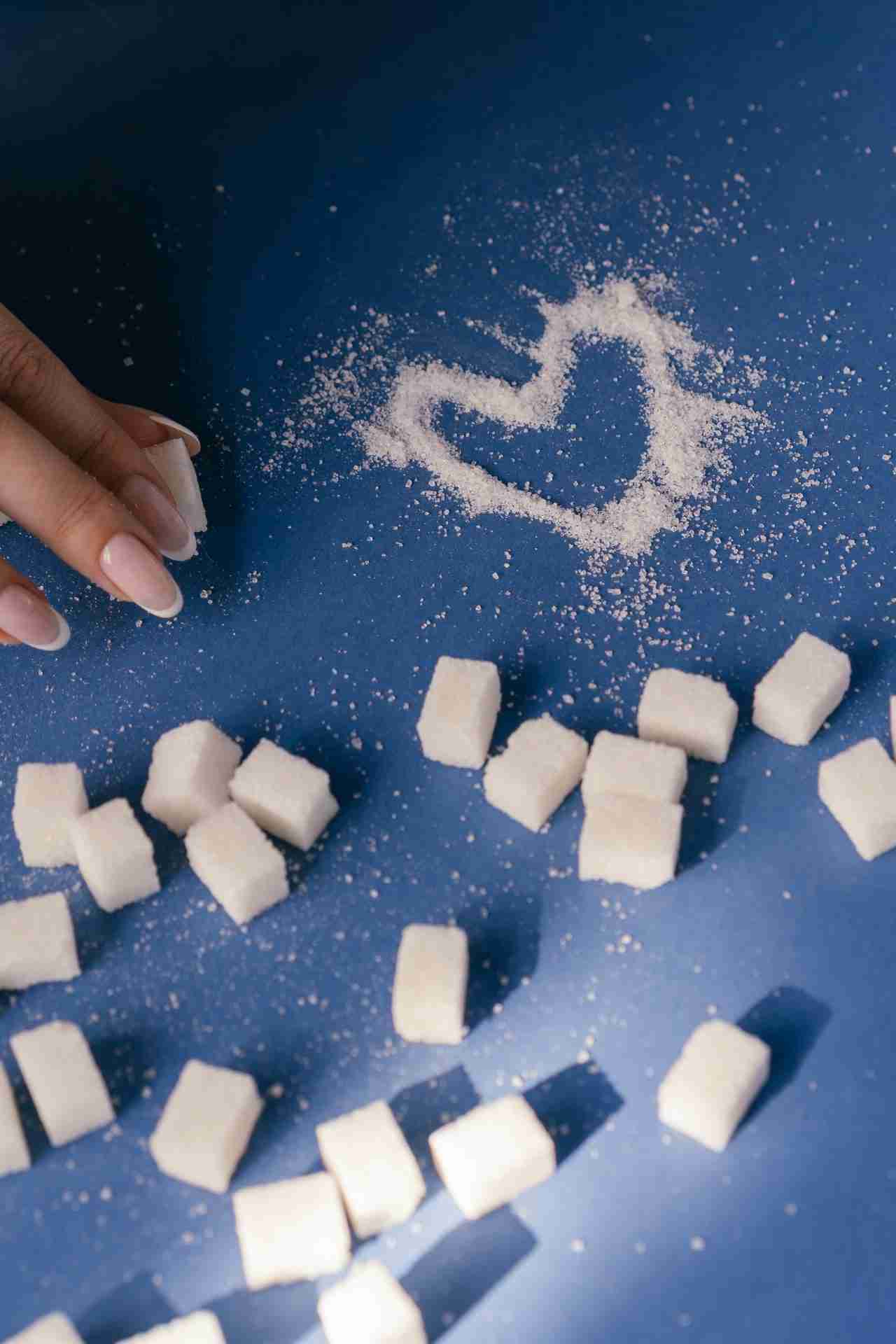 Afbeelding bij blog: is suiker verslavend? Suikerklontjes met suikerkorrels in de vorm van een hartje ernaast op een blauwe tafel